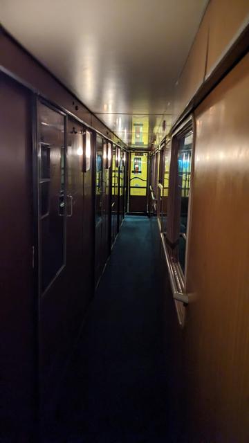 Corridor of a night train with wooden walls and low light.