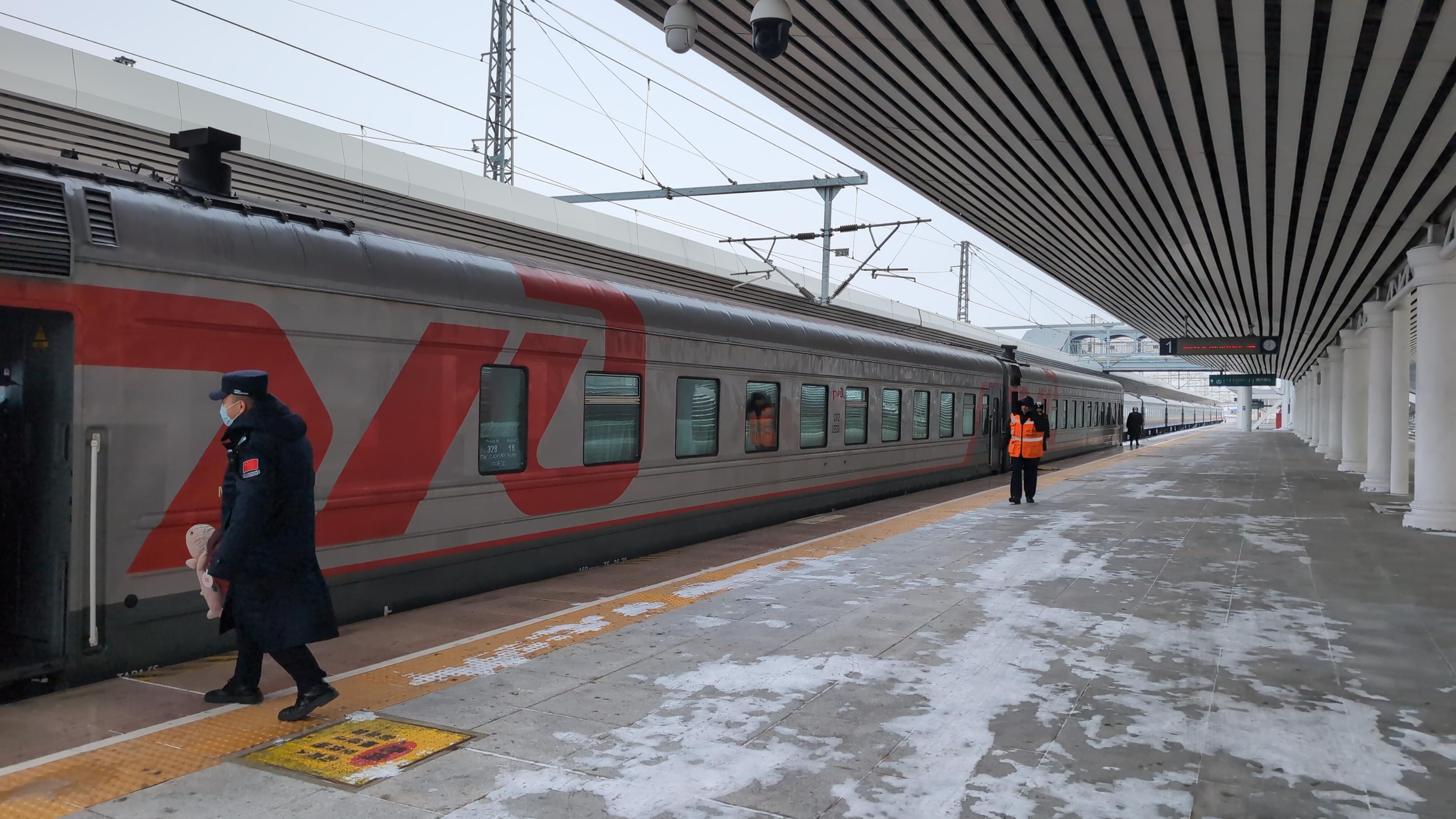 Two RZhD carriages in a snowy railway station. Notably a Chinese border officer carries Rosåhaj to the open entrance door of the carriage.